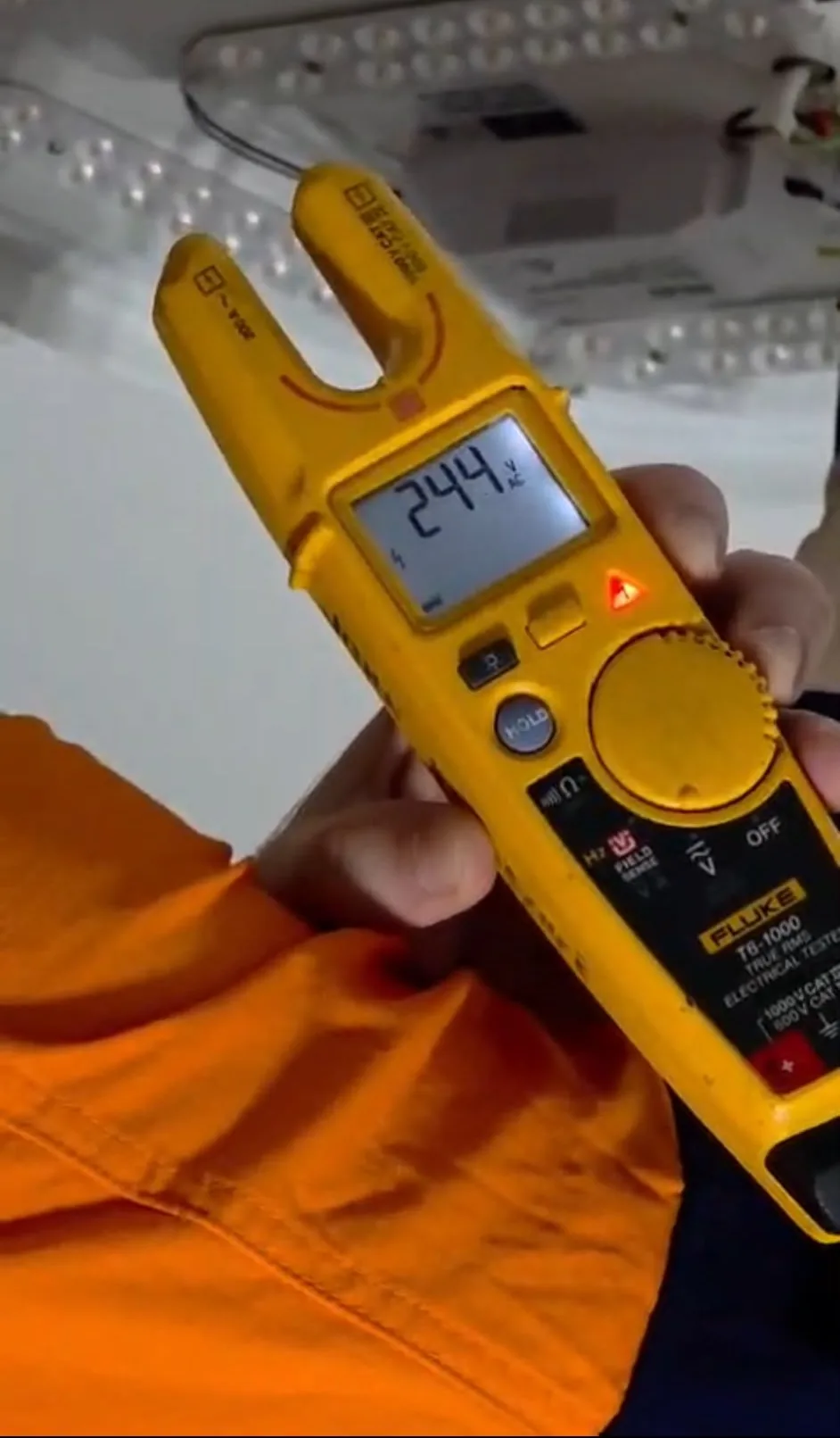 Electrician holding a Fluke voltage tester showing 244 volts at a ceiling light - Cairns City Electrics, Cairns