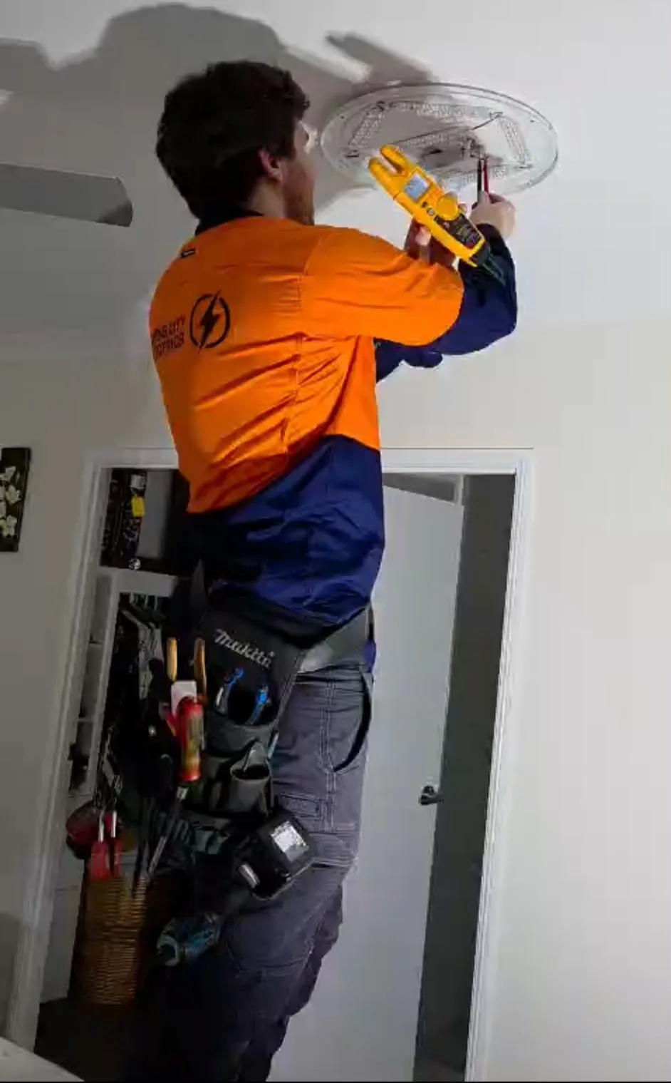 Electrician on a ladder testing a new ceiling LED light fitting inside a home - Cairns City Electrics, Cairns