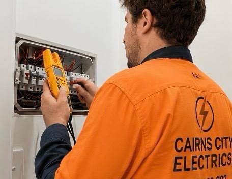 Electrician in branded shirt testing switchboard circuit breakers with a yellow multimeter - Cairns City Electrics, Cairns