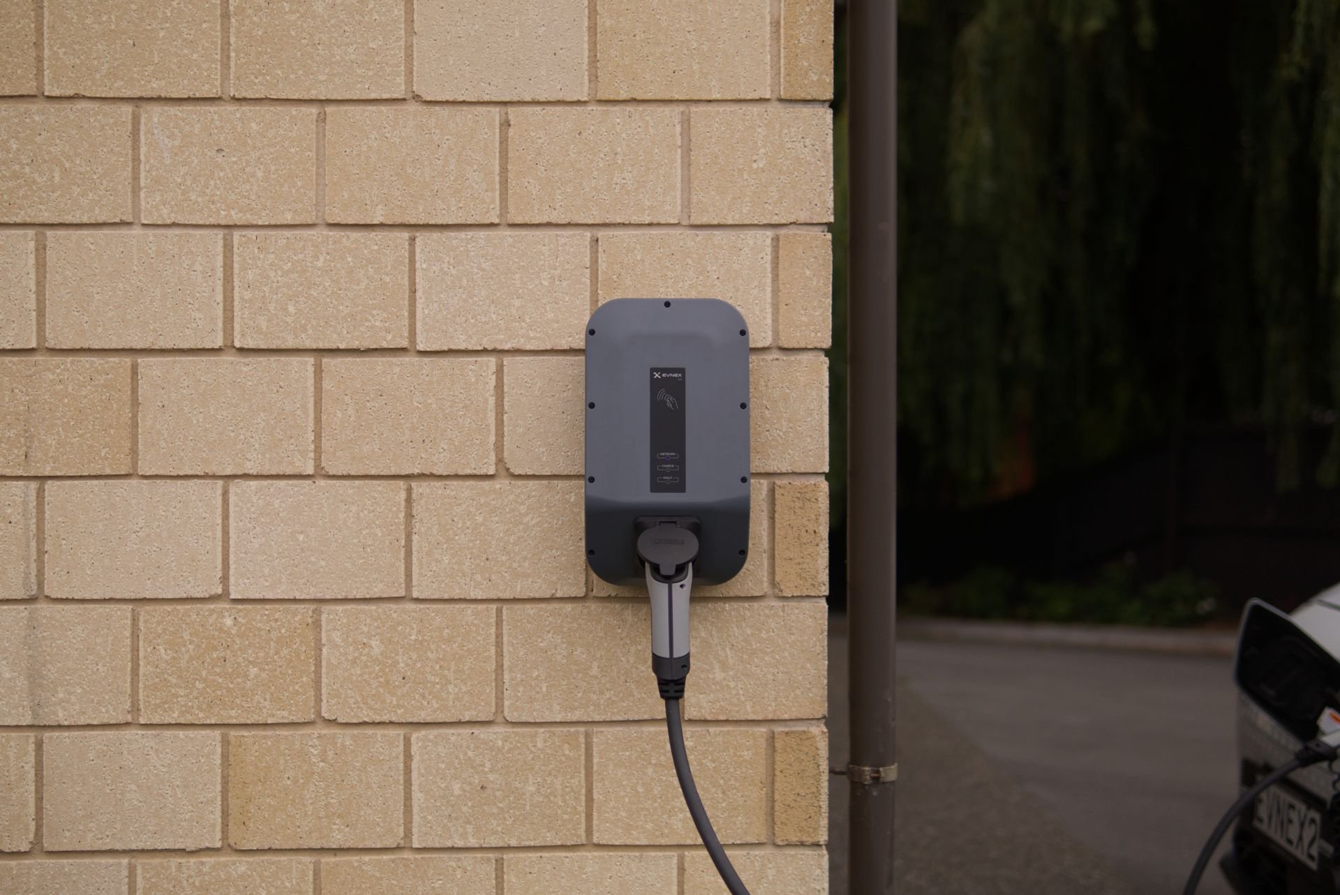 Wall-mounted home EV charger plugged in beside a driveway on a brick wall - Cairns City Electrics, Cairns